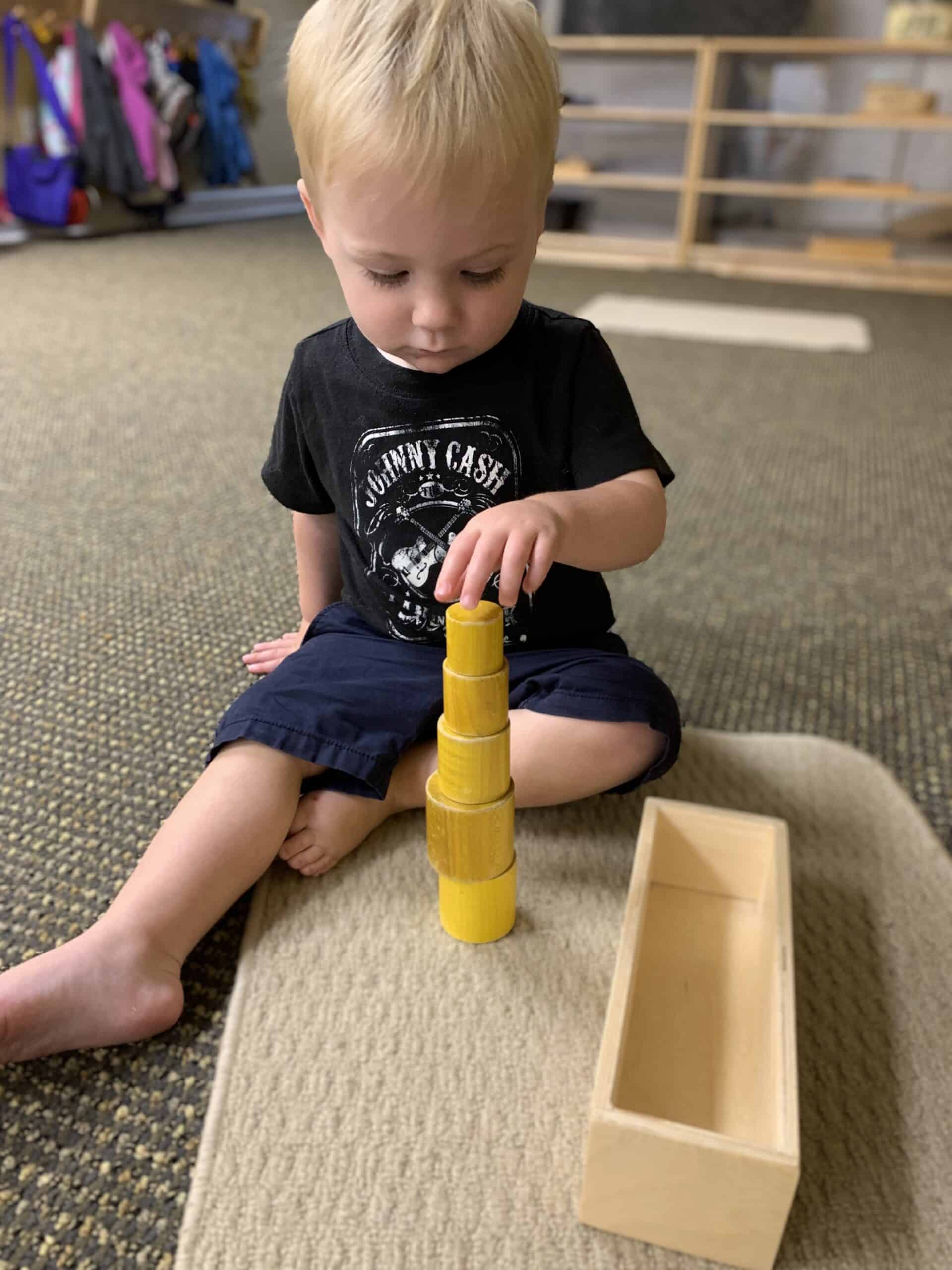 Young boy playing with stacking yellow Montessori cylinders in classroom at Mount Clemens MI daycare & preschool, practicing fine motor skills and concentration.