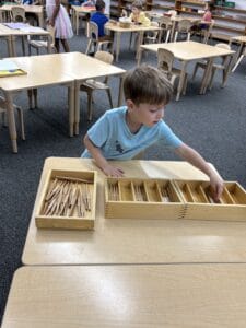 A young boy organizing wooden carving tools on a light wooden table in a Montessori classroom at Mount Clemens, MI.