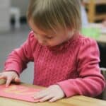 Close up of a preschool child tracing the cursive sandpaper letter 'm' to build muscle memory for writing.