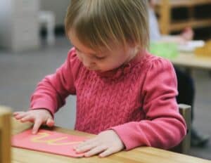 Close up of a preschool child tracing the cursive sandpaper letter 'm' to build muscle memory for writing.