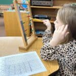 Child using large bead frame to develop math skills in Montessori education setting.