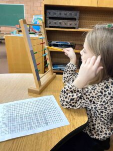 Child using wooden abacus to develop math skills in Montessori education setting.