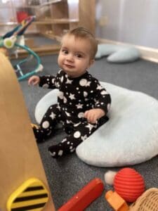 A happy infant sitting on a soft light blue cushion in a peaceful Montessori Nido environment, surrounded by developmental toys at a Mount Clemens daycare facility.