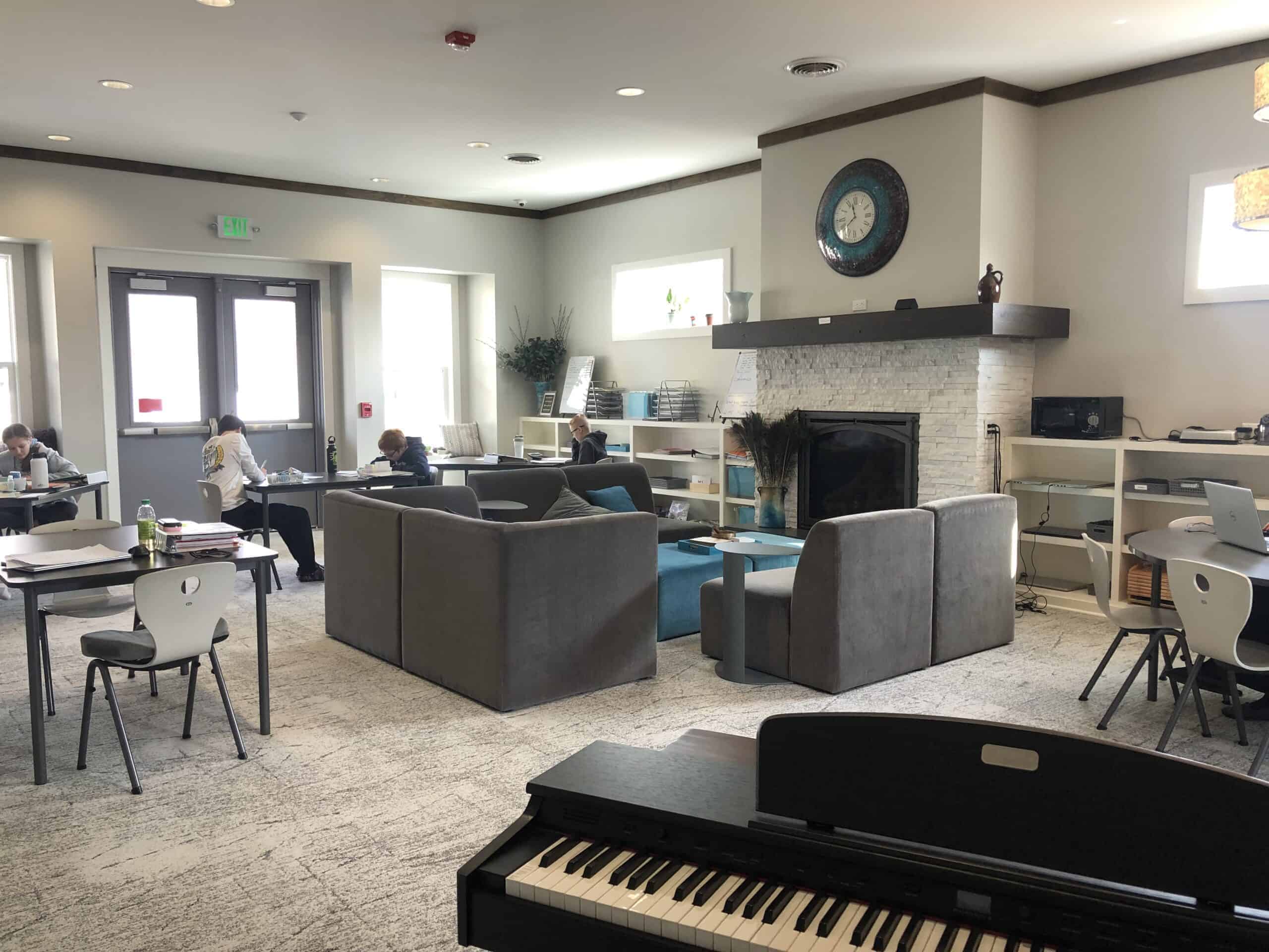 Montessori Middle School Environment | Collaborative Learning Space A spacious and modern Montessori middle school classroom in Mount Clemens, MI, featuring flexible seating, a piano, and students working at collaborative stations in a home-like environment.