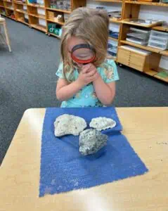 Preschool student using a magnifying glass to examine fossils and rocks during a Montessori science nature lesson.