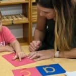 A Montessori teacher at Montessori Stepping Stones in Mount Clemens, MI guiding a young child one-on-one through a phonics lesson, reflecting the Montessori principle of following each child's individual pace