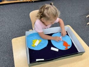 A young toddler girl at Montessori Stepping Stones concentrating on placing a pink continent piece onto a felt Montessori geography hemisphere map.