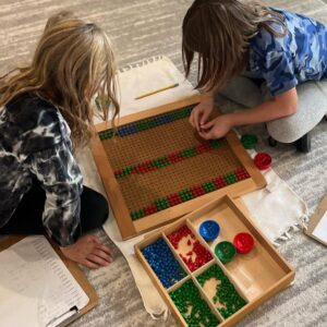 Two students working together on a Montessori math rug using beads and boards for advanced multiplication in Mount Clemens, MI.