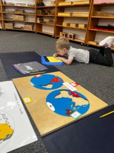 A kindergarten student at Montessori Stepping Stones in Mount Clemens, MI deeply focused on a geography lesson using the Continents of the Earth puzzle map.