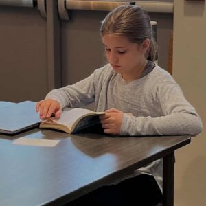 Young girl focused on reading a book at Montessori Stepping Stones elementary in Mount Clemens, MI, promoting early childhood literacy and learning.